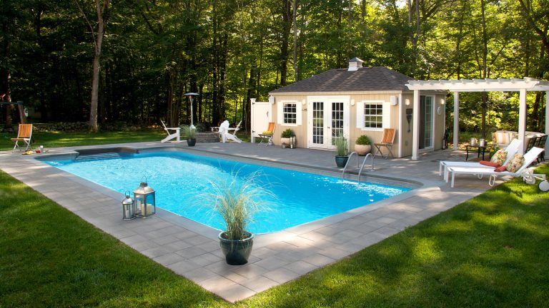 A beautiful backyard with a pool house, pergola, outdoor shower and a fire pit. Perfect for entertaining on a warm summer afternoon.