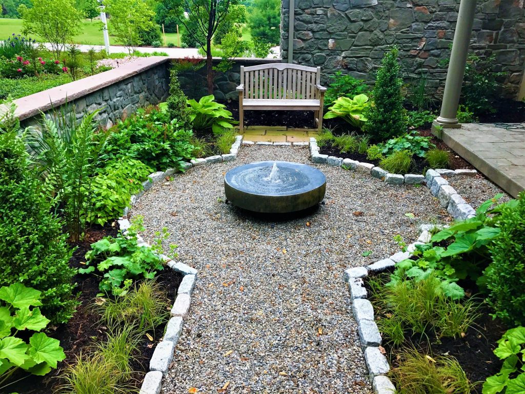 A flagstone patio and natural stone seat wall lead to a larger space including a pavilion and outdoor kitchen.