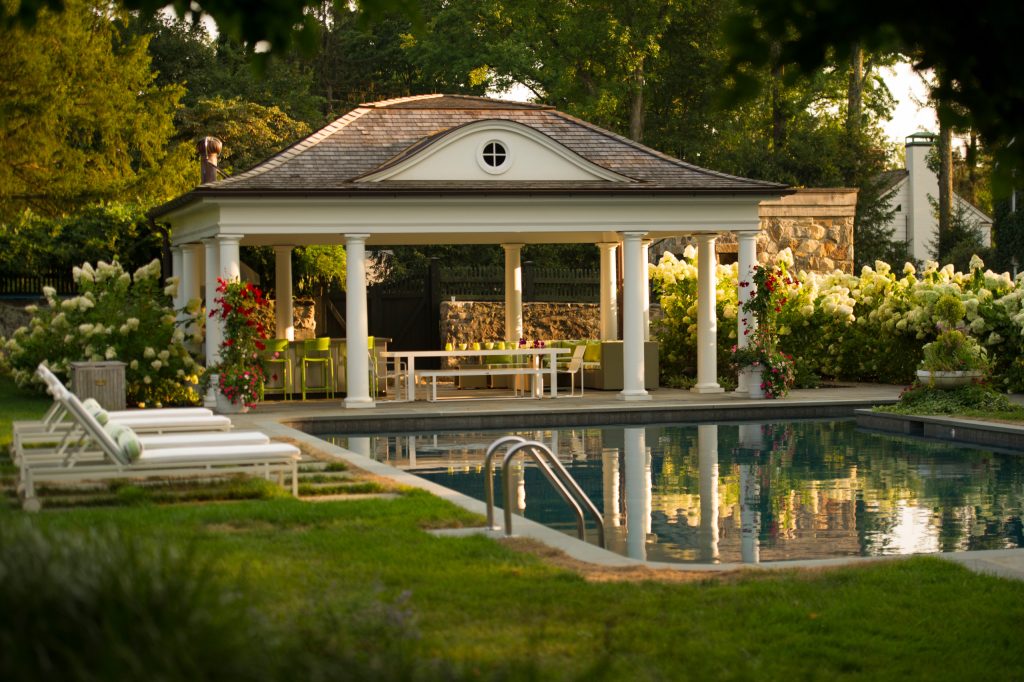 A generous three season pool house provides shelter for an outdoor kitchen, dining area, and living room.