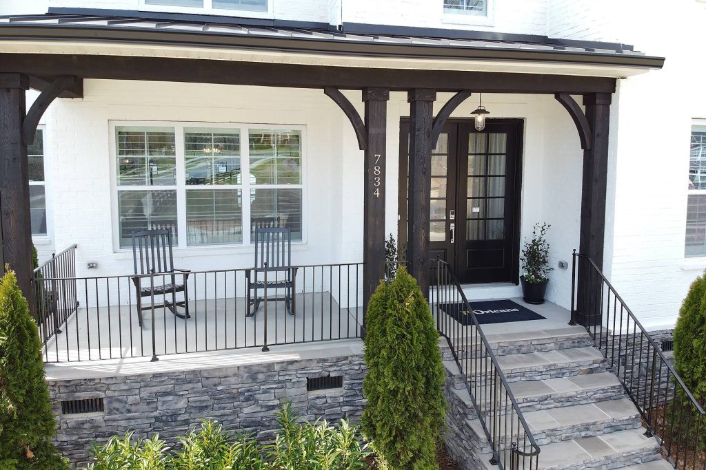 A medium sized front porch in Charlotte with dark stained wood columns and a white painted brick facade.