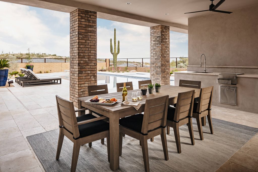A neutral ombre rug pairs well with the sleek teakwood dining table and chairs. Highlighting the natural tones seen in the scenery around, makes for a seamless patio design.