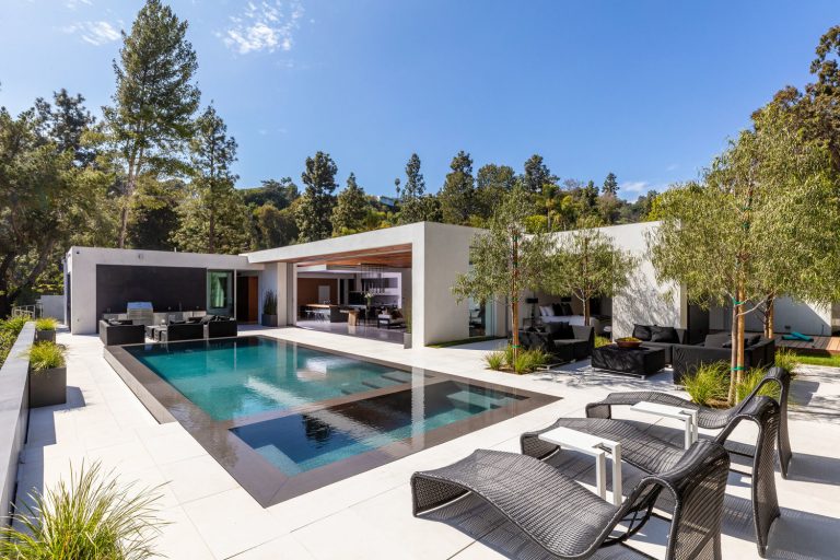 A serene backyard oasis features an infinity-edge pool and spa, gourmet Kalamazoo kitchen and lounge areas overlooking the lights of L.A.