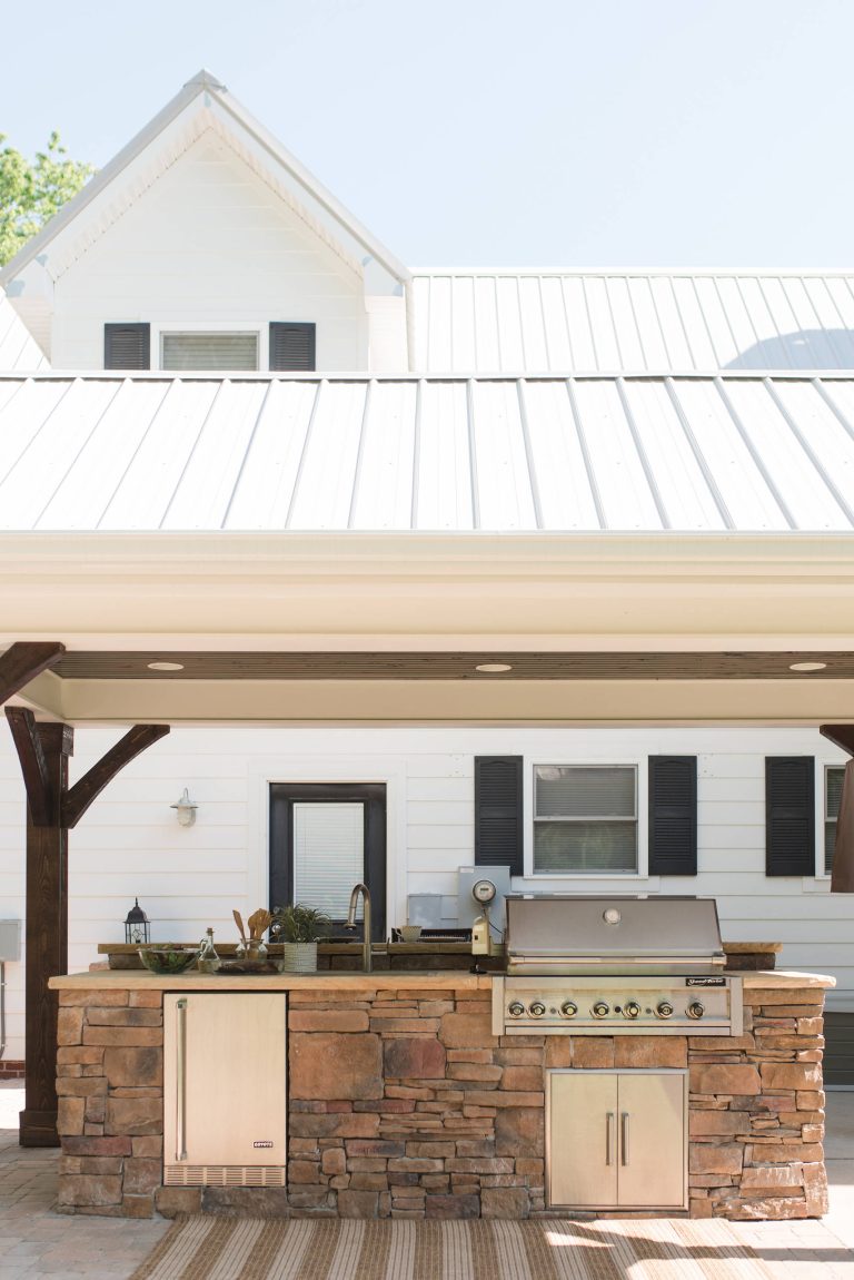Beautiful covered outdoor kitchen includes a stone island with grill, sink, and refrigerator on one side, and a raised bar with seating on the other. by Cuthbertson Homes | Outdoor Kitchens | Backyard Design | Outdoor Living Spaces | Landscape Design