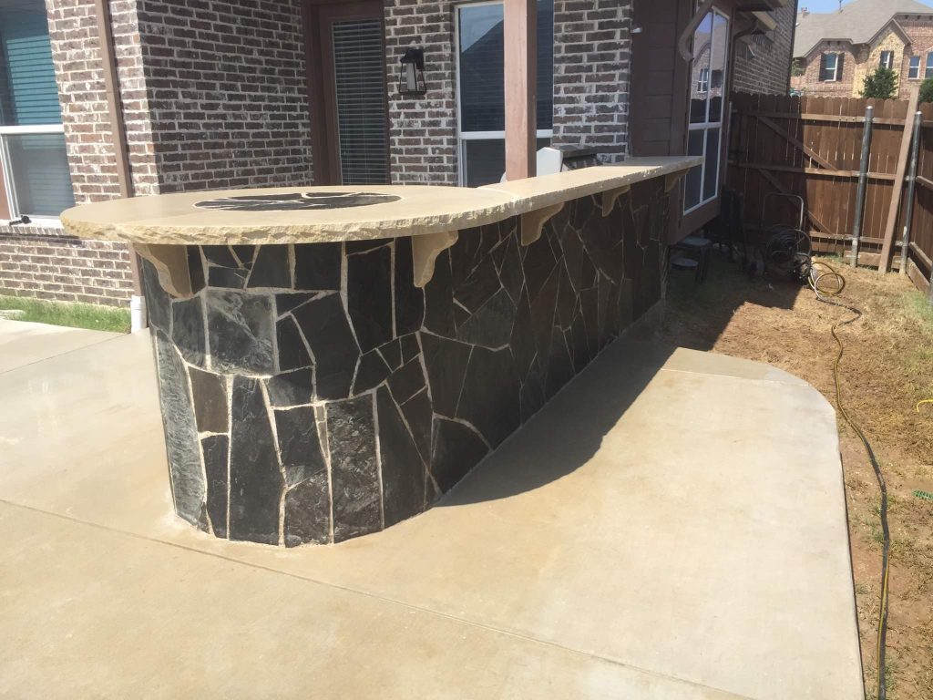 Beautiful outdoor kitchen with a round bar table designed to fit a grill and a Kamodo Joe Smoker. All sits atop of a perfectly poured, broom finished, 600+ SF concrete slab.