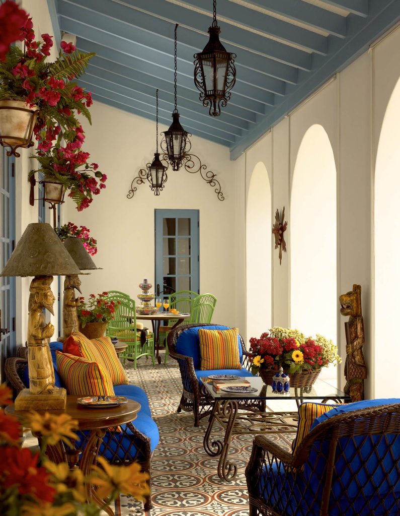 Black wrought iron pendant lantern lights are suspended from soft blue painted ceiling beams. Bright blue and yellow throw pillows adorn wicker chairs. The brightly patterned floors are Mexican tile. by GIL WALSH INTERIORS | Outdoor Photos | Porch | Landscaping | Landscape Design | Outdoor Living Space | Porch Design Ideas | Outdoor Living Space Ideas | Backyard Design