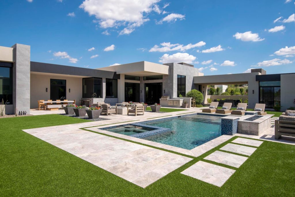Above and Beyond is the third residence in a four-home collection in Paradise Valley, Arizona. Originally the site of the abandoned Kachina Elementary School, the infill community, appropriately named Kachina Estates, embraces the remarkable views of Camelback Mountain.

Nestled into an acre sized pie shaped cul-de-sac lot, the lot geometry and front facing view orientation created a remarkable privacy challenge and influenced the forward facing facade and massing. An iconic, stone-clad massing wall element rests within an oversized south-facing fenestration, creating separation and privacy while affording views “above and beyond.”

Above and Beyond has Mid-Century DNA married with a larger sense of mass and scale. The pool pavilion bridges from the main residence to a guest casita which visually completes the need for protection and privacy from street and solar exposure.

The pie-shaped lot which tapered to the south created a challenge to harvest south light. This was one of the largest spatial organization influencers for the design. The design undulates to embrace south sun and organically creates remarkable outdoor living spaces.

This modernist home has a palate of granite and limestone wall cladding, plaster, and a painted metal fascia. The wall cladding seamlessly enters and exits the architecture affording interior and exterior continuity.

Kachina Estates was named an Award of Merit winner at the 2019 Gold Nugget Awards in the category of Best Residential Detached Collection of the Year. The annual awards ceremony was held at the Pacific Coast Builders Conference in San Francisco, CA in May 2019.

Project Details: Above and Beyond
Architecture: Drewett Works
Developer/Builder: Bedbrock Developers
Interior Design: Est Est
Land Planner/Civil Engineer: CVL Consultants
Photography: Dino Tonn and Steven Thompson

Awards:
Gold Nugget Award of Merit - Kachina Estates - Residential Detached Collection of the Year by Drewett Works | Pool design | Pool Contracting | Swimming Pool Ideas | Swimming Pool Design Ideas