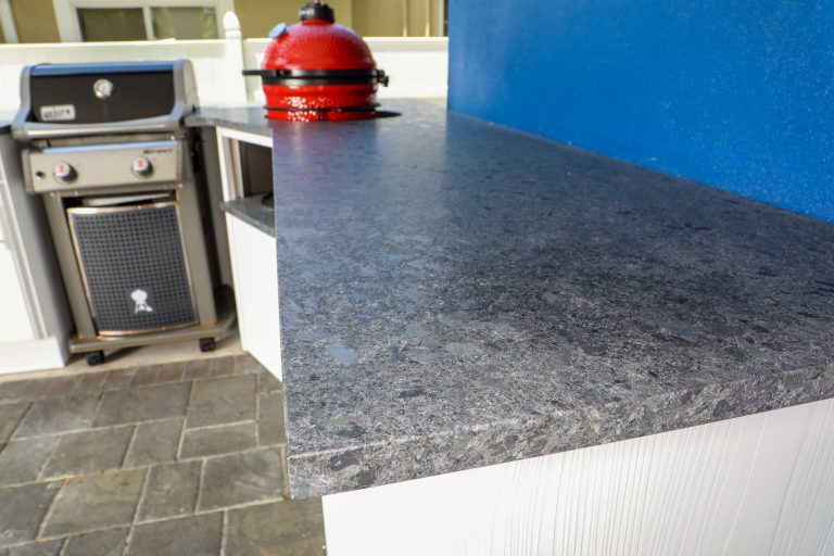 Custom outdoor kitchen and gas fire pit build on the saltwater. The outdoor kitchen features 100% weatherproof outdoor cabinets and premium smoker from Kamado Joe.