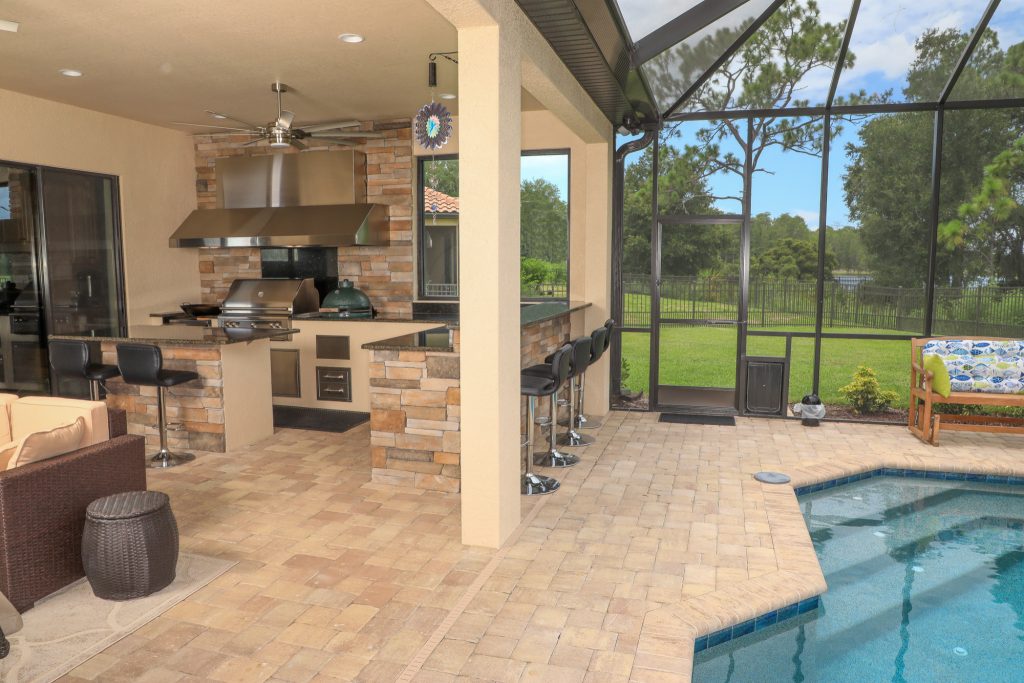Custom outdoor kitchen build featuring custom dual vent hood, gas grill, power burner, Big Green Egg grill, bar seating area and additional prep island with seating.