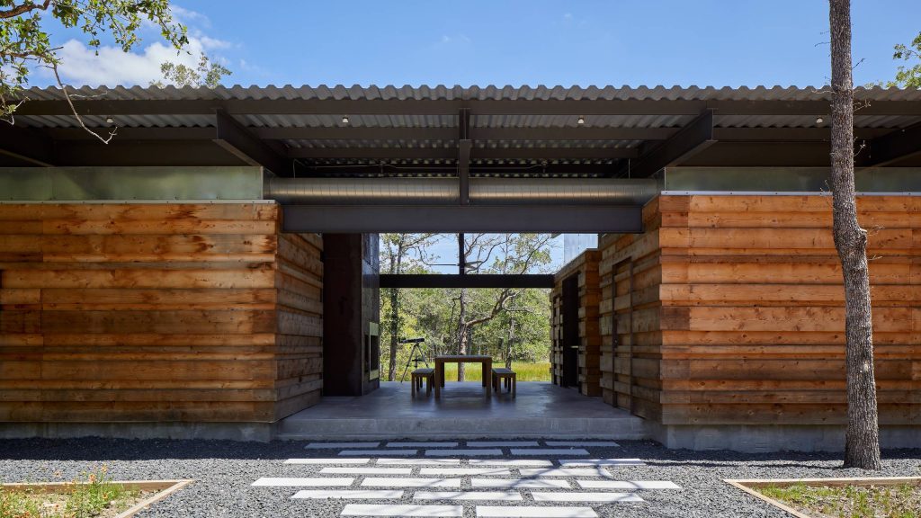 Entry approach - dog trot style large covered porch with communal dining table and exterior fireplace overlooking the big pond