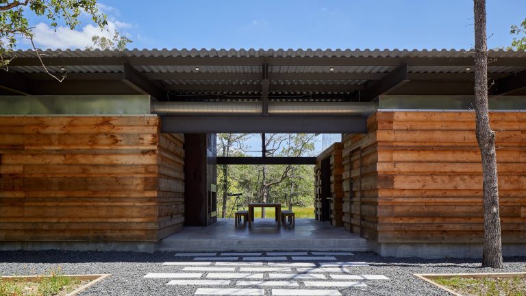 Entry approach - dog trot style large covered porch with communal dining table and exterior fireplace overlooking the big pond