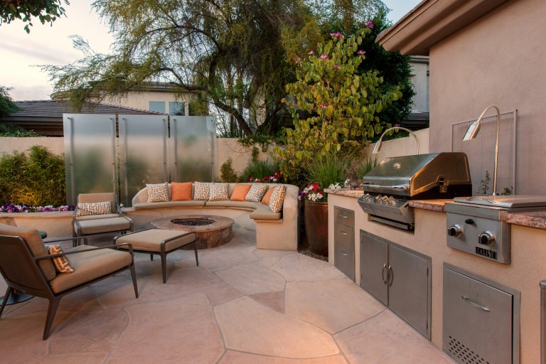 Every day is a vacation in this beautiful backyard retreat featuring comfortable inviting seating, a custom outdoor kitchen, glass privacy panels which light up at night, and stunning foilage.