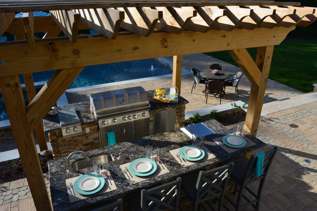 Example of a large arts and crafts backyard concrete paver patio kitchen design in Richmond with a pergola