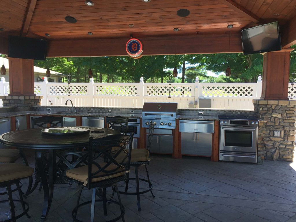 Example of a large classic backyard stamped concrete patio kitchen design in Grand Rapids with a pergola