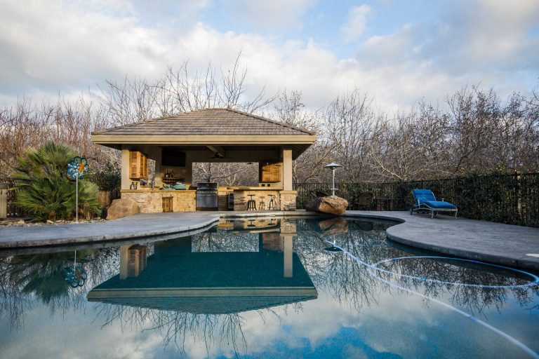 Example of a large minimalist backyard stamped concrete patio kitchen design in Other with a gazebo
