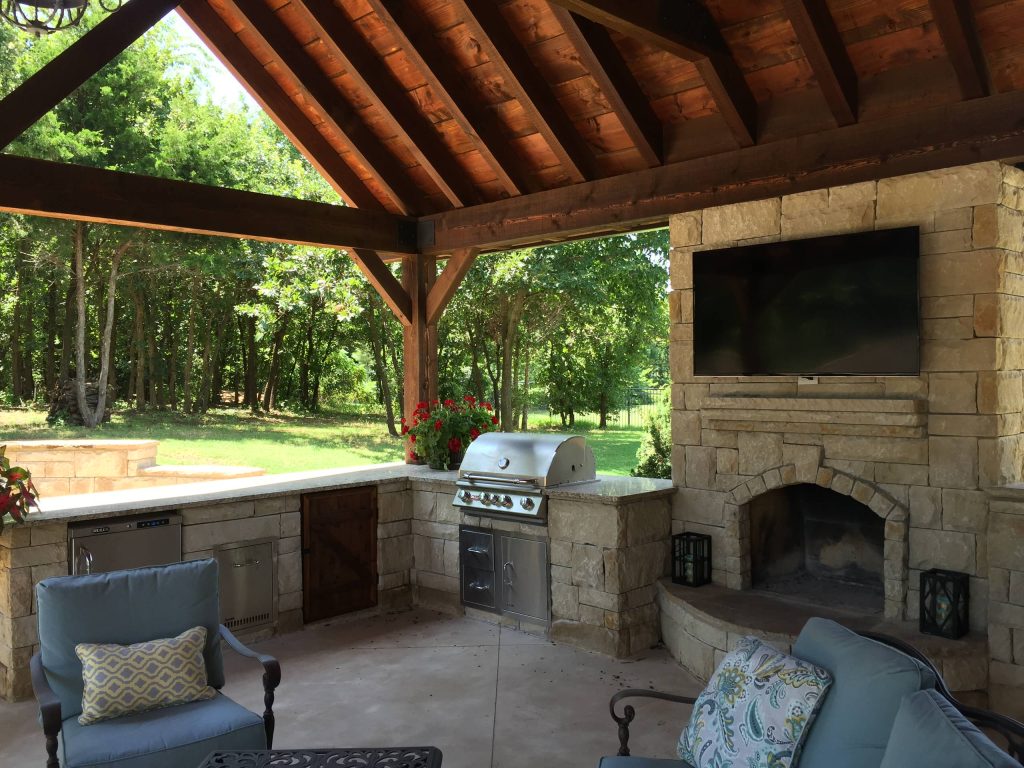 Example of a large mountain style backyard stone patio kitchen design in Orange County with a roof extension