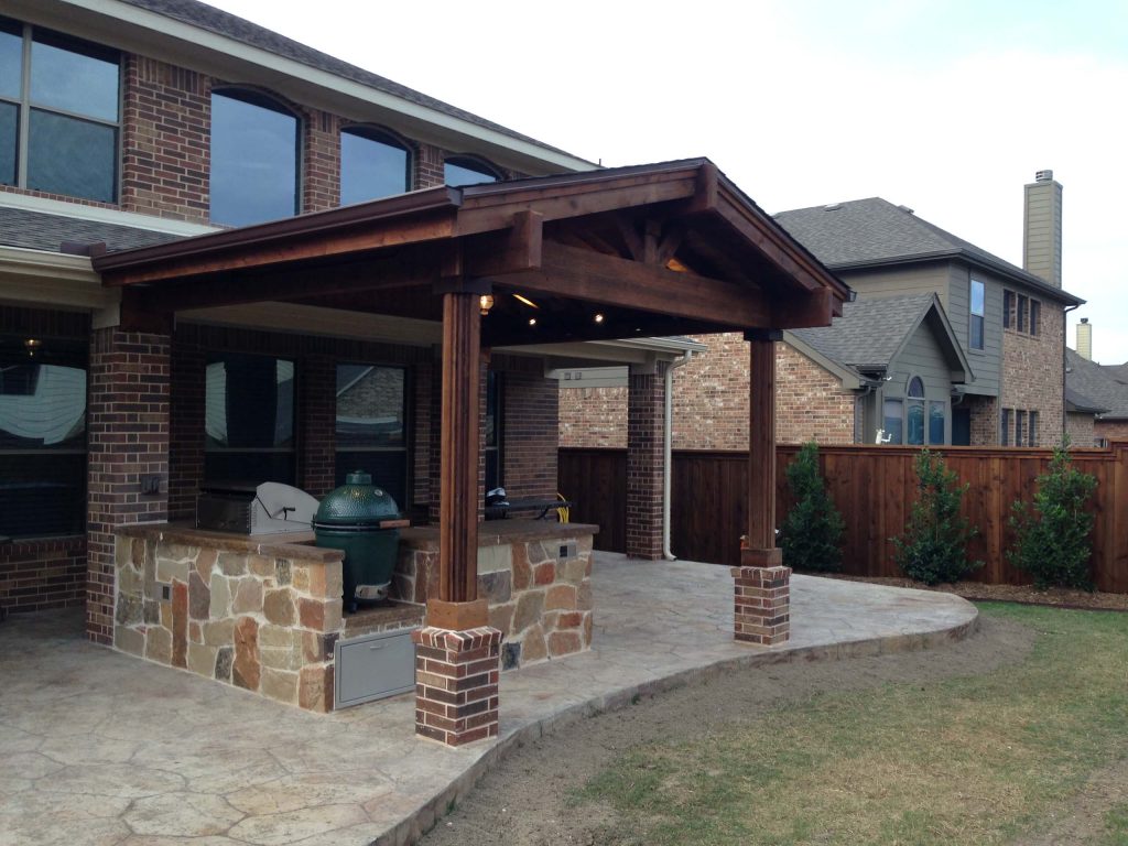 Example of a mid-sized mountain style backyard stamped concrete patio kitchen design in Dallas with an awning