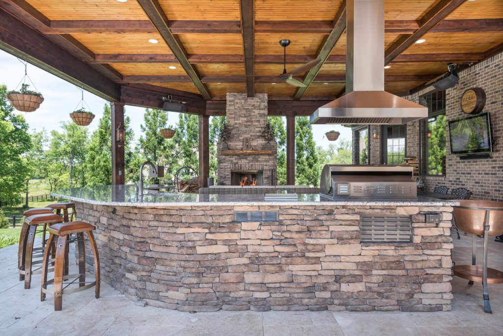 Example of a mountain style backyard stone patio kitchen design in Other with a roof extension