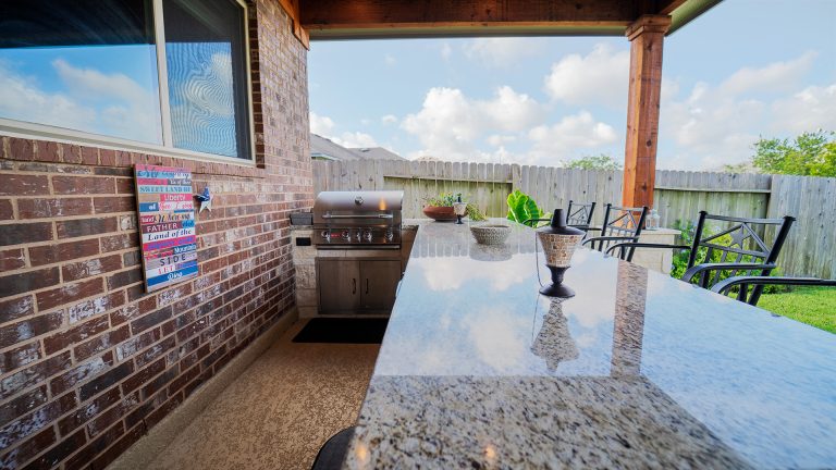 Example of a transitional backyard stamped concrete patio kitchen design in Houston with a roof extension