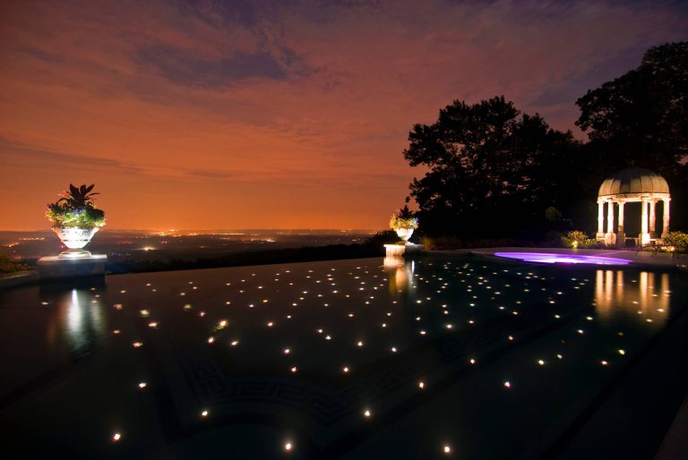 Fiber optic lights shine like stars in the sky beneath the surface of this luxurious vanishing edge swimming pool design in Alpine NJ.