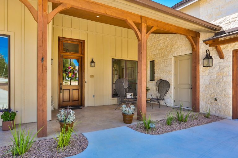 Front exterior entry. Features wood columns and ceiling, tile floor, small "desert" landscape, and outdoor living furniture.