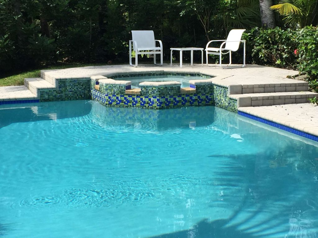 Hot tub - large tropical backyard concrete paver and custom-shaped hot tub idea in Miami