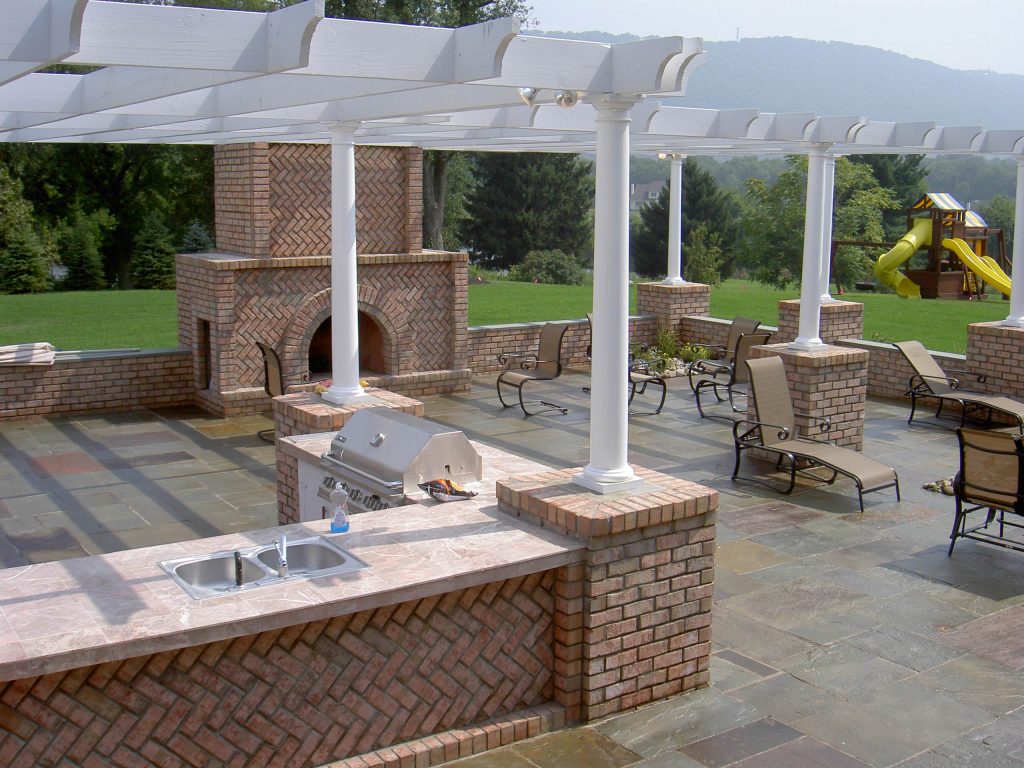Inspiration for a large timeless side yard concrete paver patio kitchen remodel in New York with a pergola
