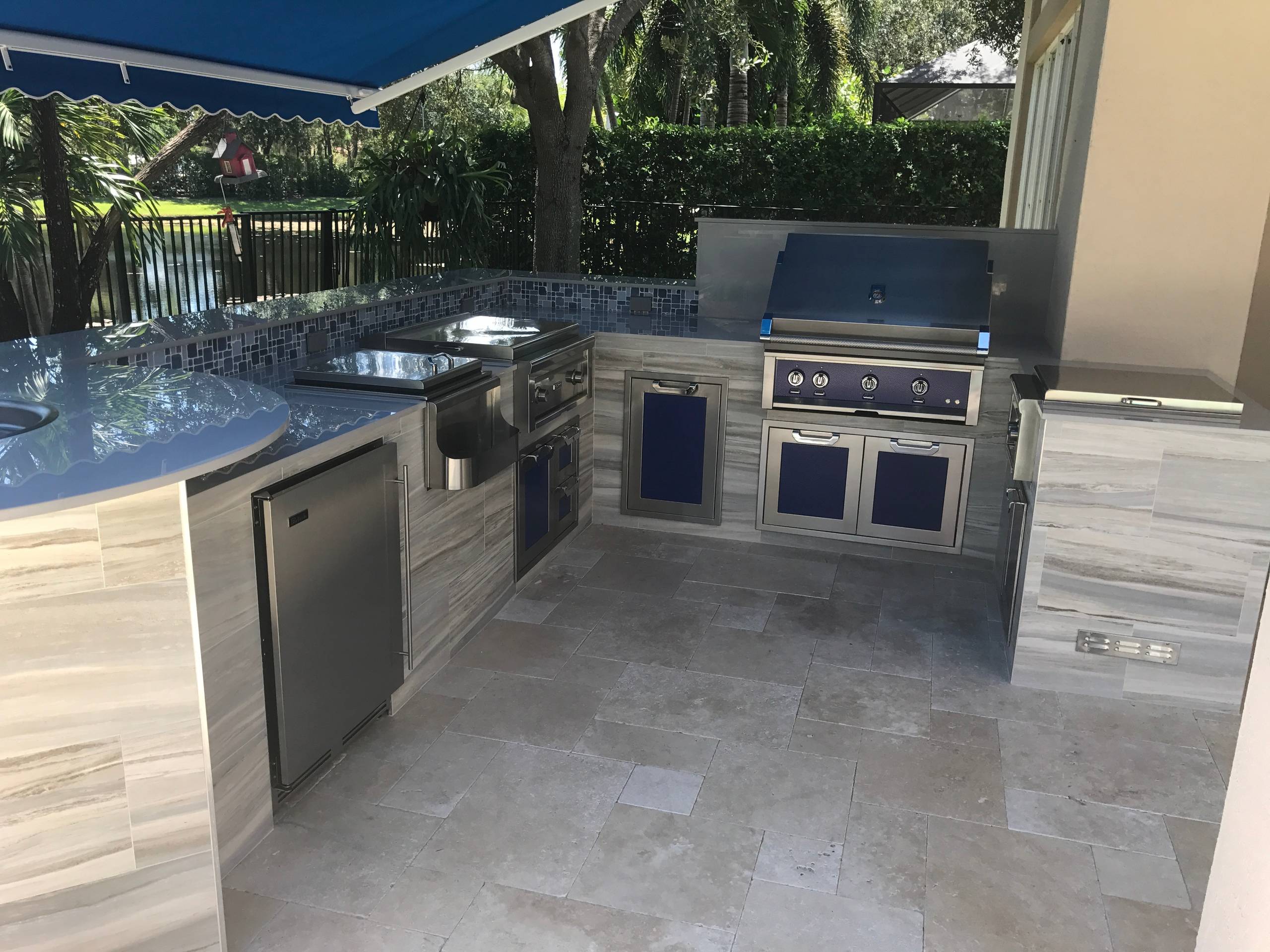 Inspiration for a tropical backyard stone patio kitchen remodel in Miami with an awning
