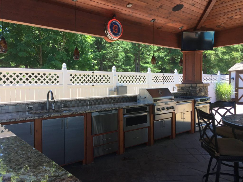 Large elegant backyard stamped concrete patio kitchen photo in Grand Rapids with a pergola