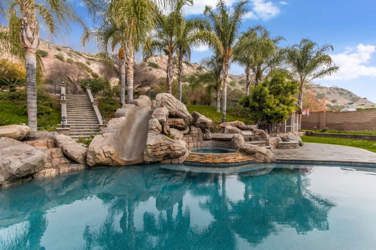 Large island style backyard concrete paver and custom-shaped water slide photo in Orange County