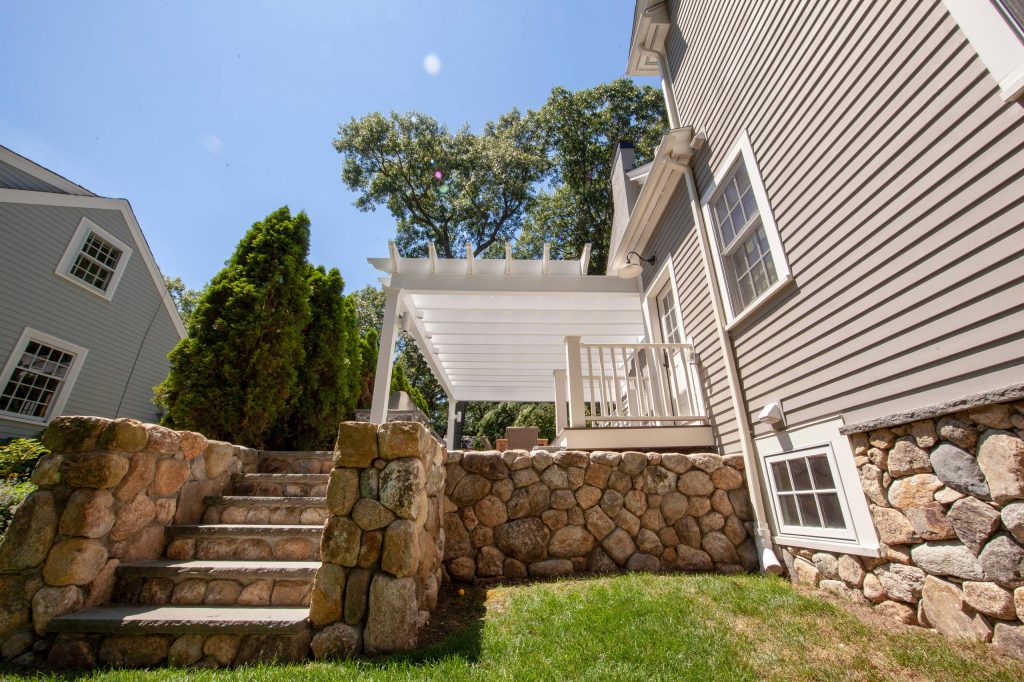 Large minimalist side yard stone patio kitchen photo in Boston with a pergola