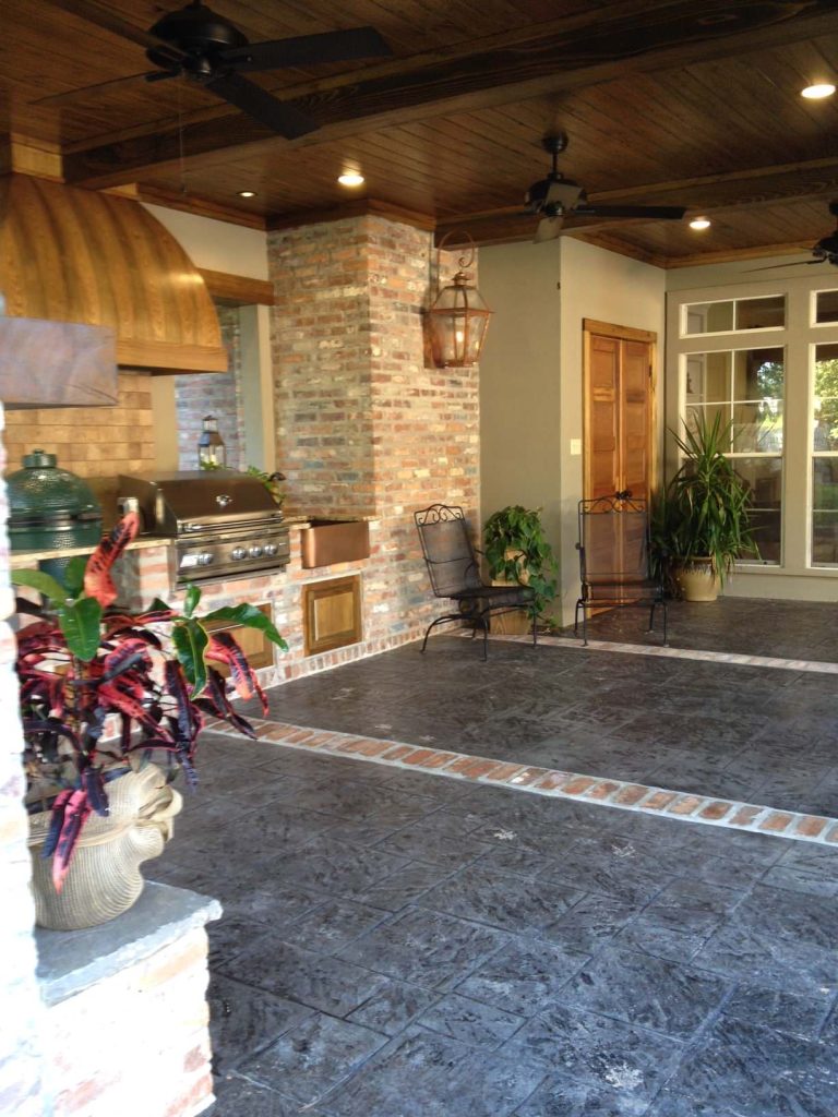 Large mountain style backyard stamped concrete patio kitchen photo in New Orleans with a roof extension