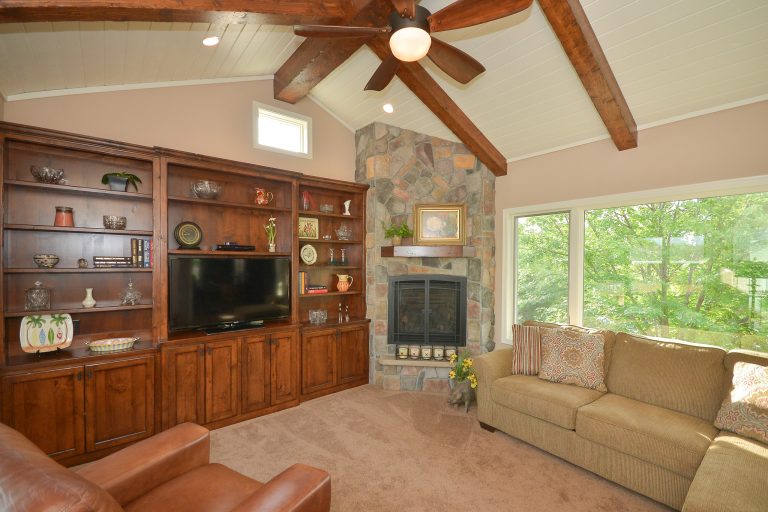 Large picture window gives view of green space, while white tongue and groove ceilings show off exposed ceiling beams.Donna Mae Photography