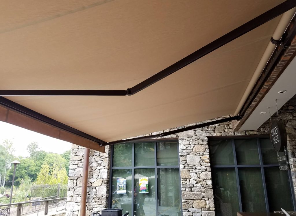 Large urban backyard stone patio kitchen photo in Other with an awning