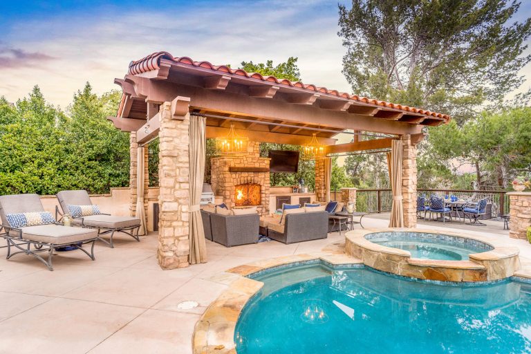Every day is a vacation in this Thousand Oaks Mediterranean-style outdoor living paradise. This transitional space is anchored by a serene pool framed by flagstone and elegant landscaping. The outdoor living space emphasizes the natural beauty of the surrounding area while offering all the advantages and comfort of indoor amenities, including stainless-steel appliances, custom beverage fridge, and a wood-burning fireplace. The dark stain and raised panel detail of the cabinets pair perfectly with the El Dorado stone pulled throughout this design; and the airy combination of chandeliers and natural lighting produce a charming, relaxed environment.

Flooring:
Kitchen and Pool Areas: Concrete
Pool Surround: Flagstone
Deck: Fiberon deck material
Light Fixtures: Chandelier
Stone/Masonry: El Dorado

Photographer: Tom Clary by JRP Design & Remodel | Pool design | Pool Contracting | Swimming Pool Ideas | Swimming Pool Design Ideas