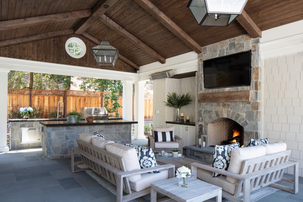 Outdoor family room with stained beams, bluestone flooring and a rock mantle.