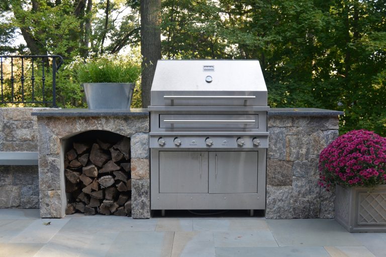 Outdoor grilling area on upper level of a bi-level patio. Kalamazoo grill with wood storage area and granite counters.