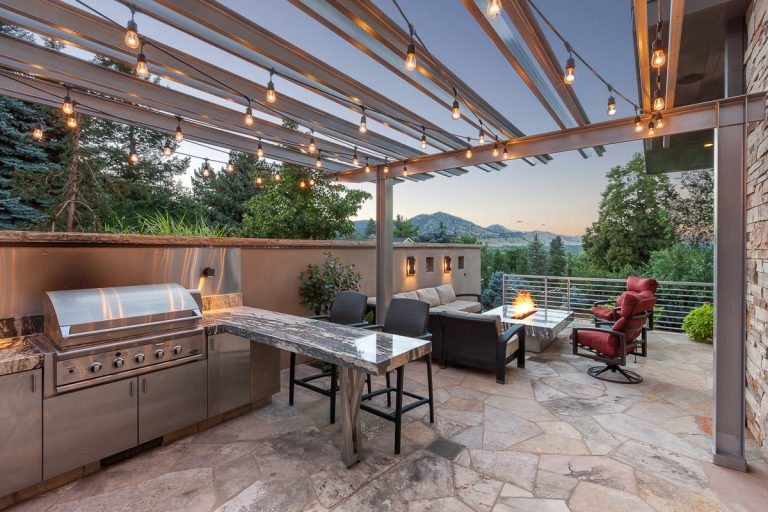 Outdoor patio features contemporary fireplace set in a stone tabletop, neutral patio furniture, stainless steel accents to pick up custom outdoor trellis. Michael deLeon