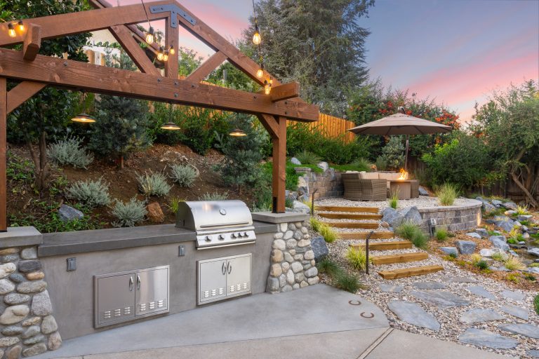 Outdoor seating area and retaining wall with prefabricated fire feature and native California plants. This design also includes a custom outdoor kitchen with a freestanding pergola.