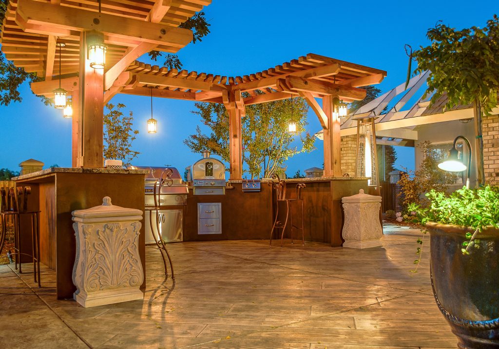 Patio kitchen - huge rustic backyard stone patio kitchen idea in Other with a pergola