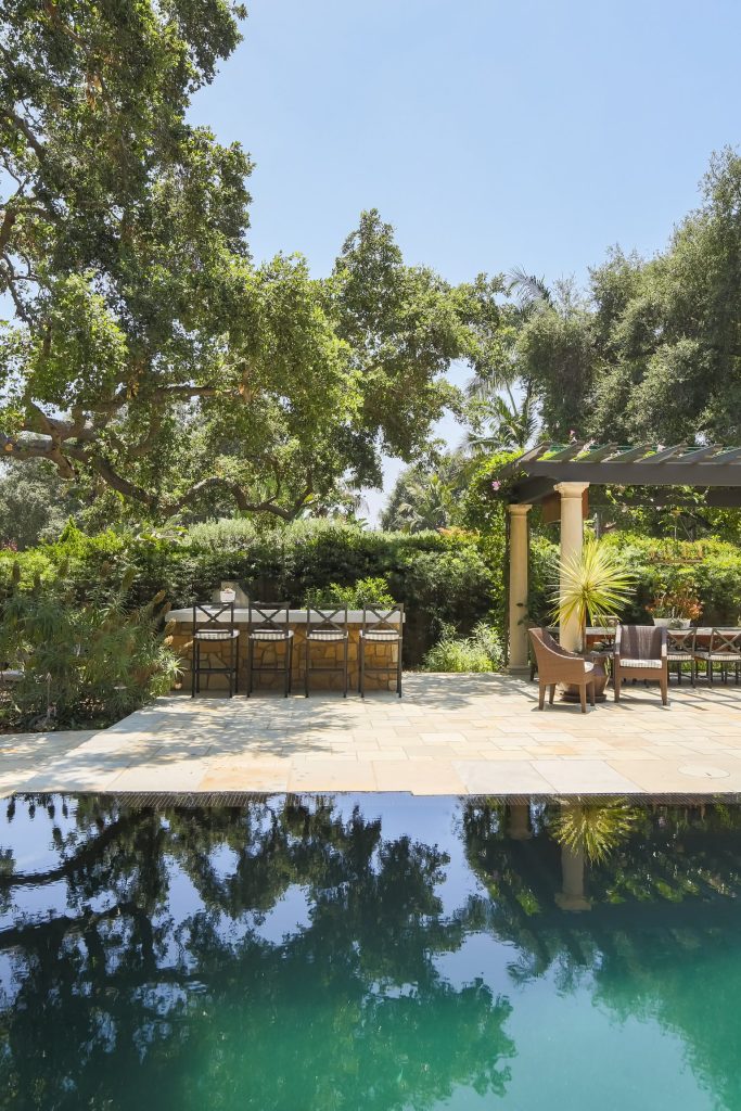 Patio kitchen - large mediterranean backyard stone patio kitchen idea in Los Angeles with a pergola