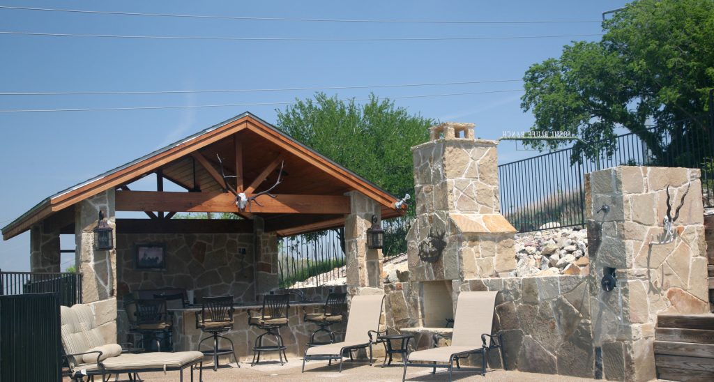 Patio kitchen - large rustic backyard stone patio kitchen idea in Dallas with an awning