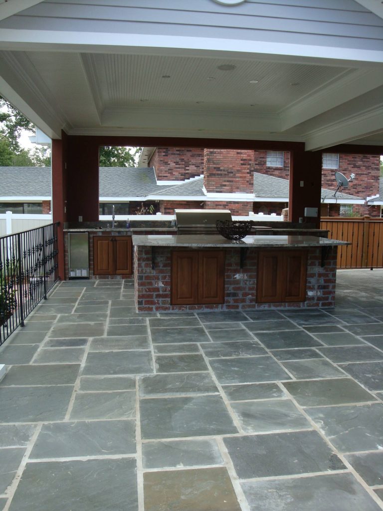 Patio kitchen - large traditional backyard stone patio kitchen idea in New Orleans with a roof extension