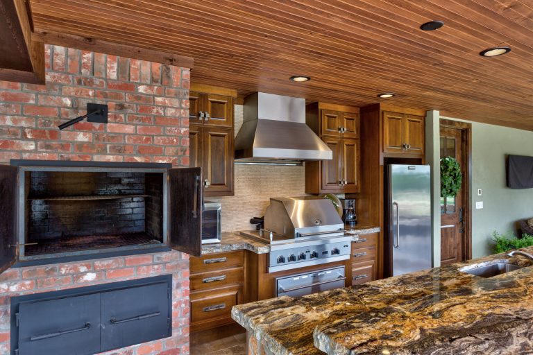 Pool house with rock bar, island and fireplace. Brick smoker and custom cabinetry. Brick privacy wall. Photo Credits: Epic Foto Group