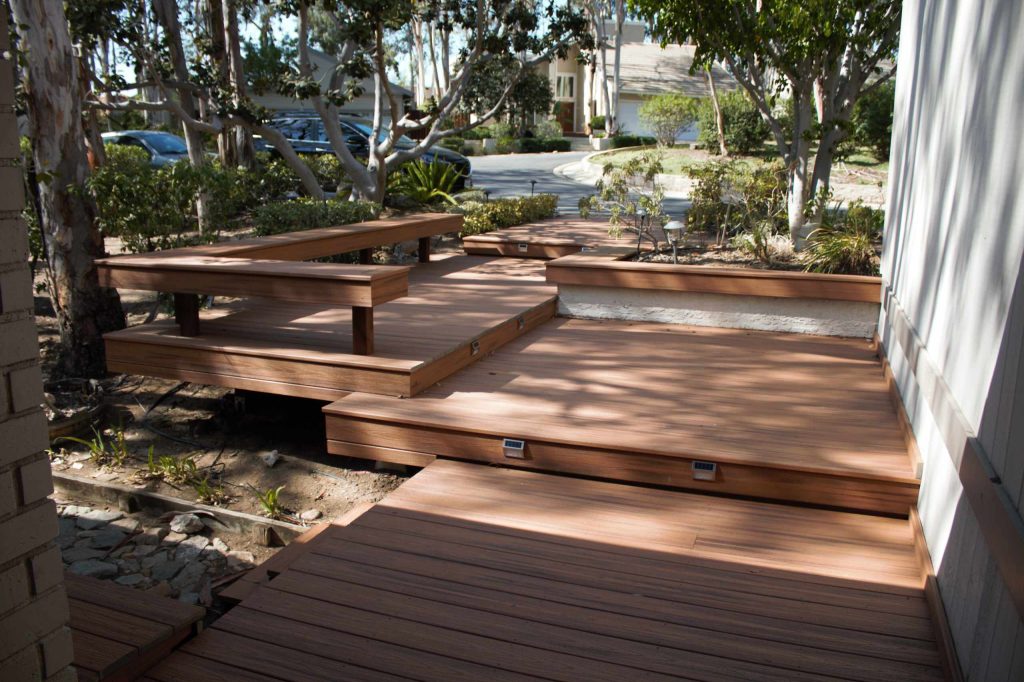 Redwood deck with grey stain on hill with glass railing and redwood posts.
