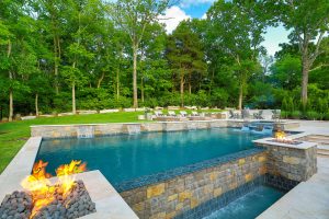 Reverse infinity-edge pool with spa, fire features, sheer descents, and travertine paver decking.