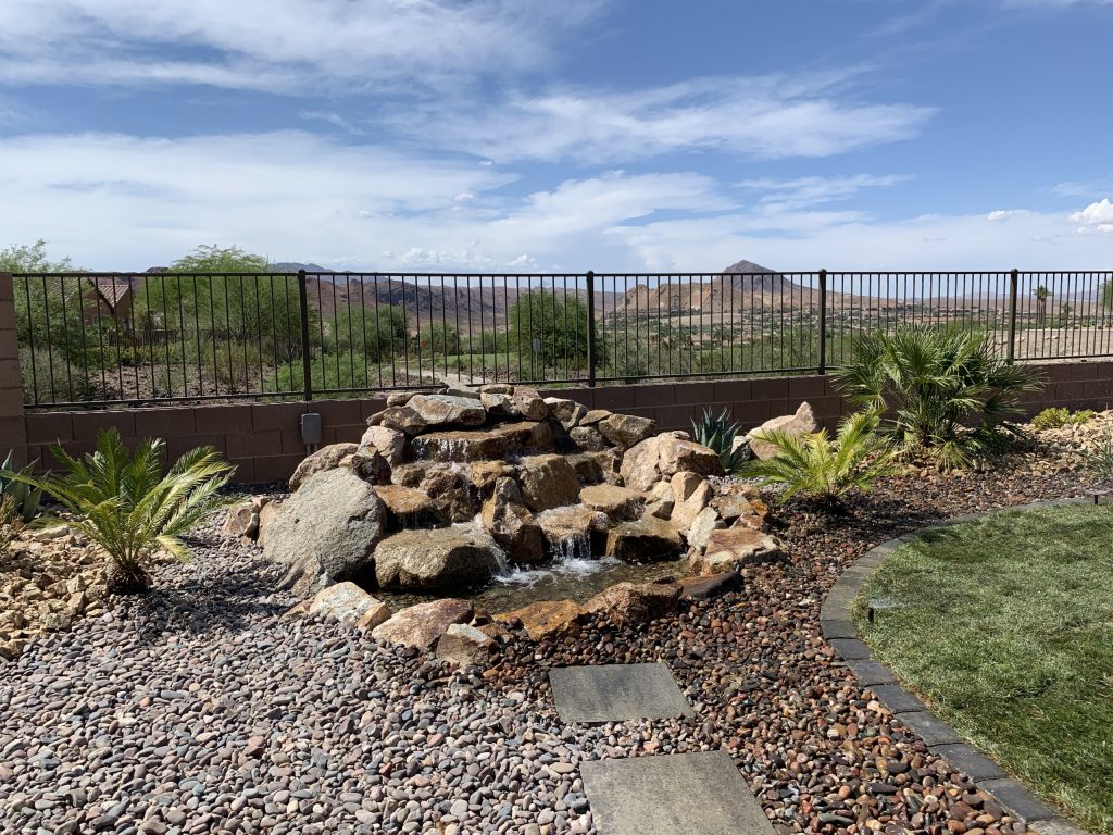 Rustic modern landscape and patio area in Lake Las Vegas, NV. A non-linear design, natural grass, and custom built rock waterfall feature compliment the extraordinary view.