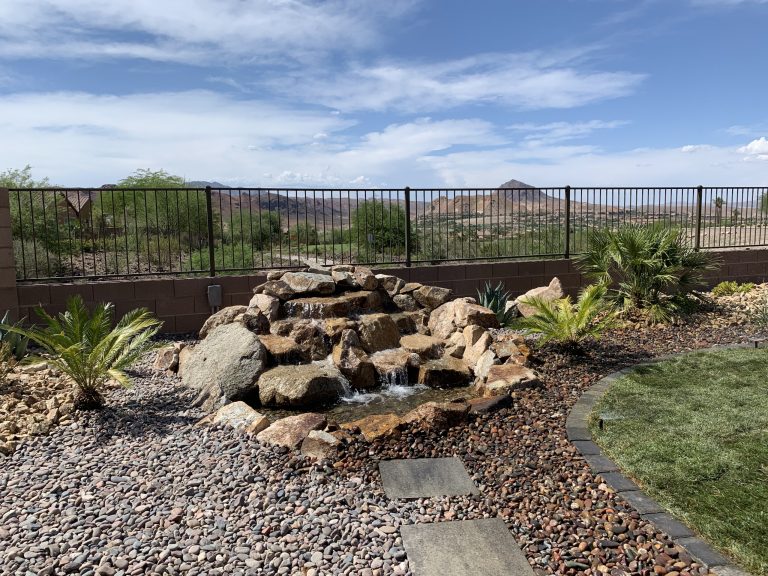 Rustic modern landscape and patio area in Lake Las Vegas, NV. A non-linear design, natural grass, and custom built rock waterfall feature compliment the extraordinary view.