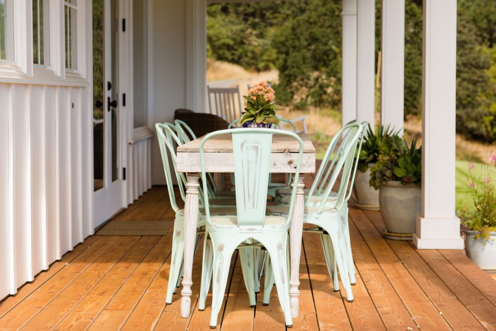 Rustic outdoor living table and chairs on a covered, wraparound porch.