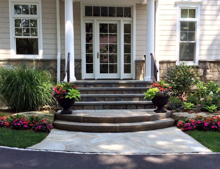 Side entrance stoop framed by seasonal planters. The large ornamental grass screens a hose bib from the visitors' view.