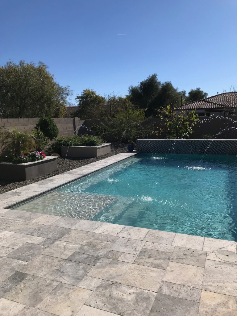 Silver Travertine pool pavers provide a cool surface and a beautiful look for this sleek pool.